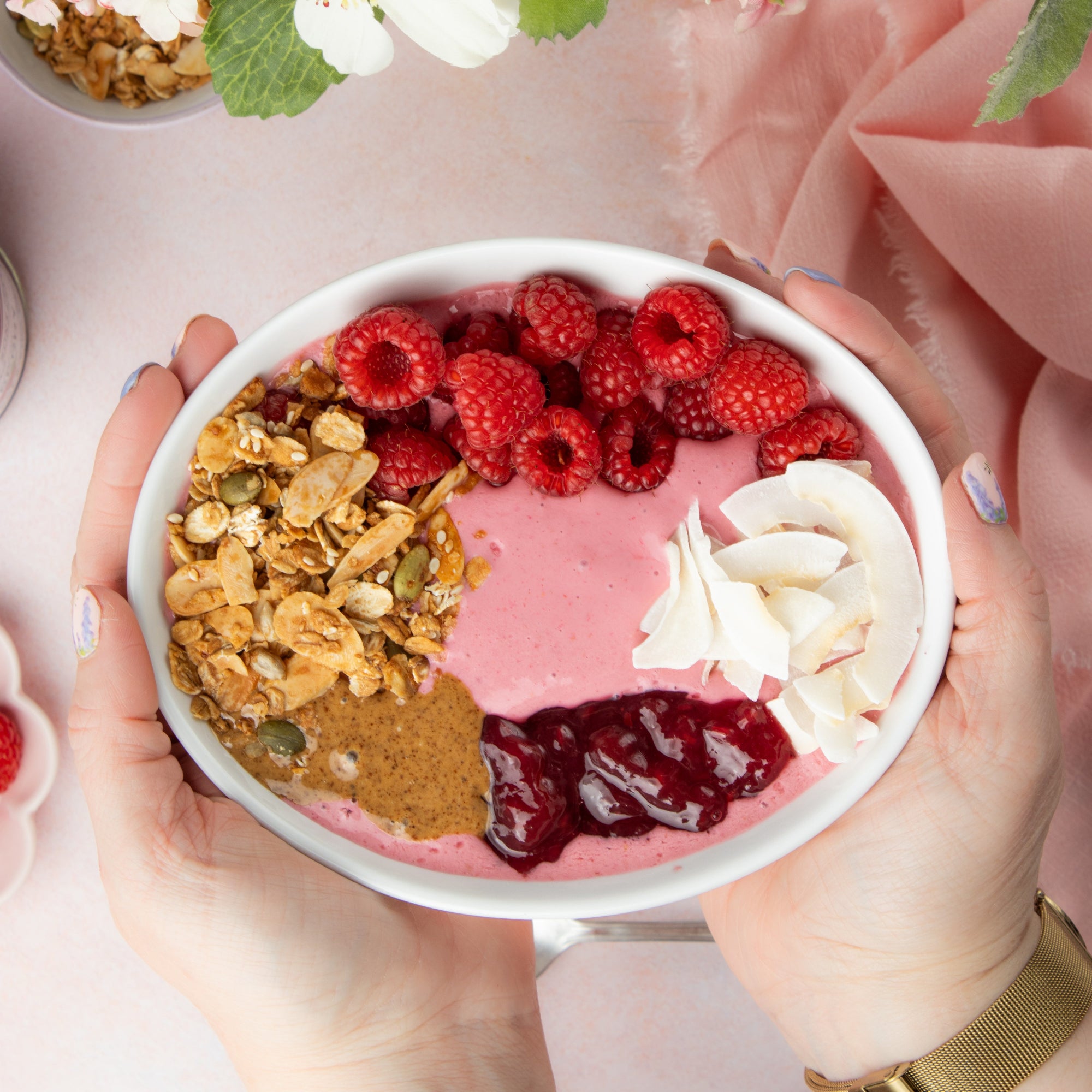 Person holding a bowl of yoghurt smoothie with toppings on a light pink background