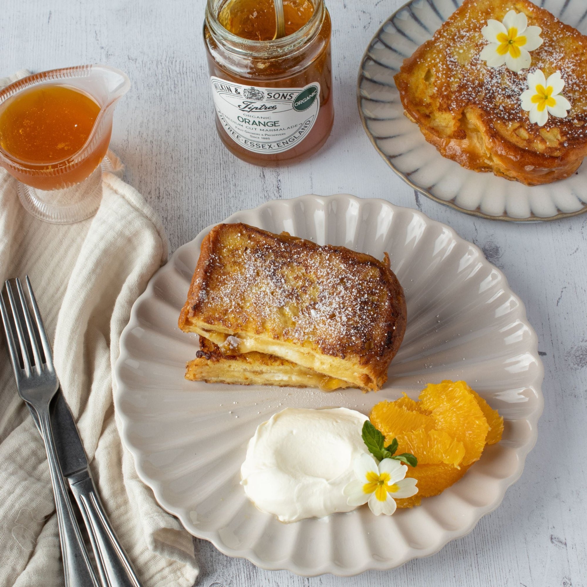 French toast with whipped cream and orange segments on a white plate, accompanied by a jar of organic marmalade.