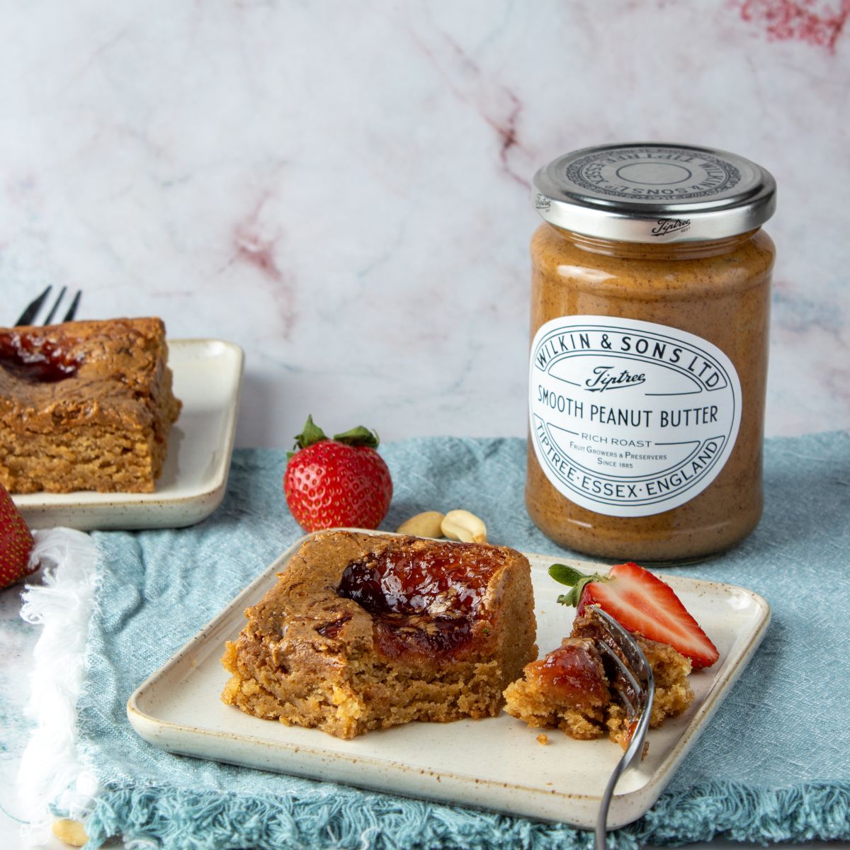 Jar of peanut butter with a blondie on a plate, set against a marble background