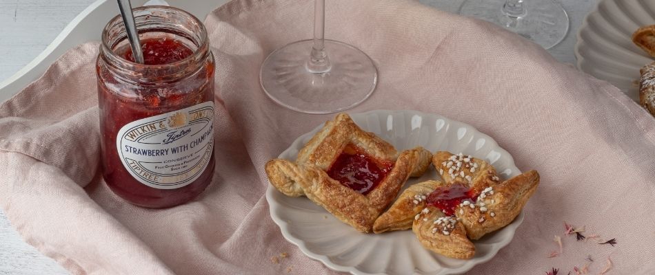 A jar of Tiptree Strawberry with Champagne Conserve next to a freshly baked mini pastry