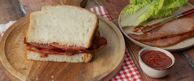 A bacon sandwich on white bread with a small pot of Tiptree Tomato Ketchup and lettuce off to one side.