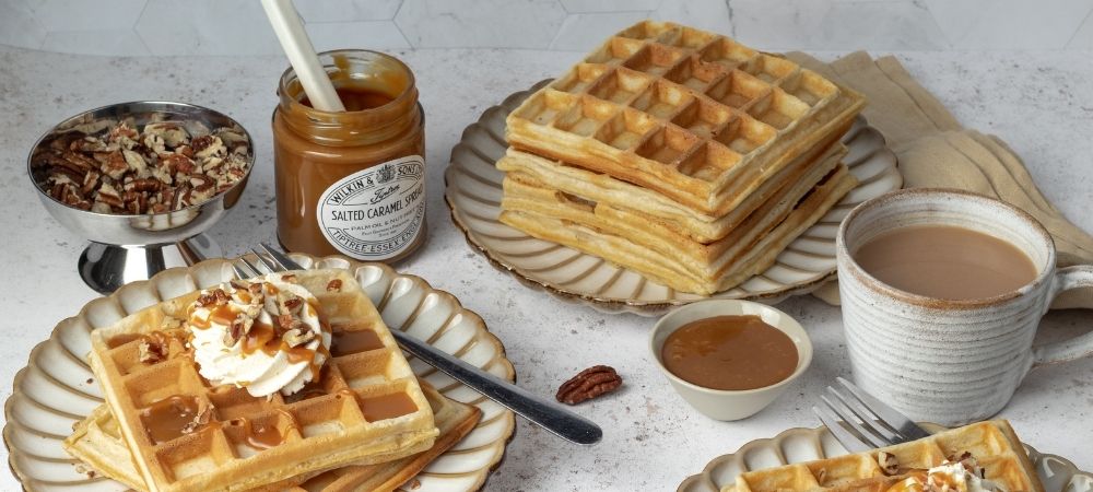 Plates of waffles with pecans and a jar of Tiptree Salted Caramel spread