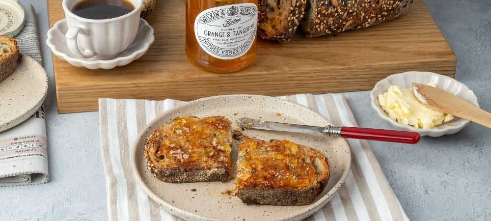Tiptree Orange and Tangerine Marmalade on Toast, next to an open jar and a cup of tea.