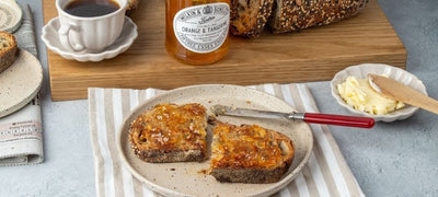 Tiptree Orange and Tangerine Marmalade on Toast, next to an open jar and a cup of tea.