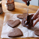 Person spreading chocolate on heart-shaped cookies on a wooden surface