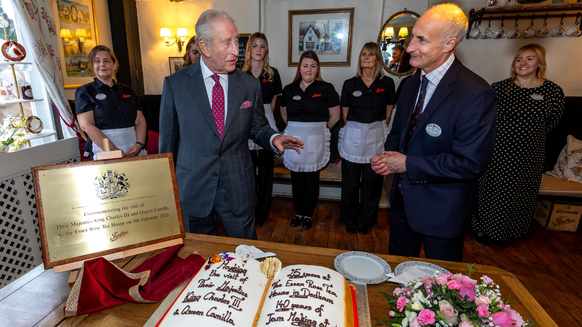 His Majesty King Charles II and Tiptree staff standing next to a large cake with a plaque.