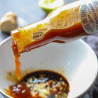 Tiptree Hot Mango Sauce being poured into a bowl with ingredients.