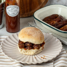 Sausage Bap with brown sauce on a plate next to a bottle of Wilkin & Son's Tiptree brown sauce.