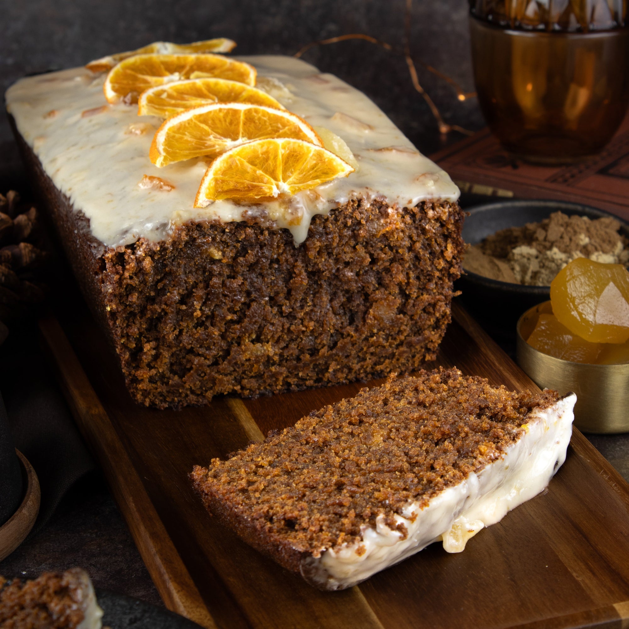 Loaf of cake with white frosting and orange slices on a wooden board.