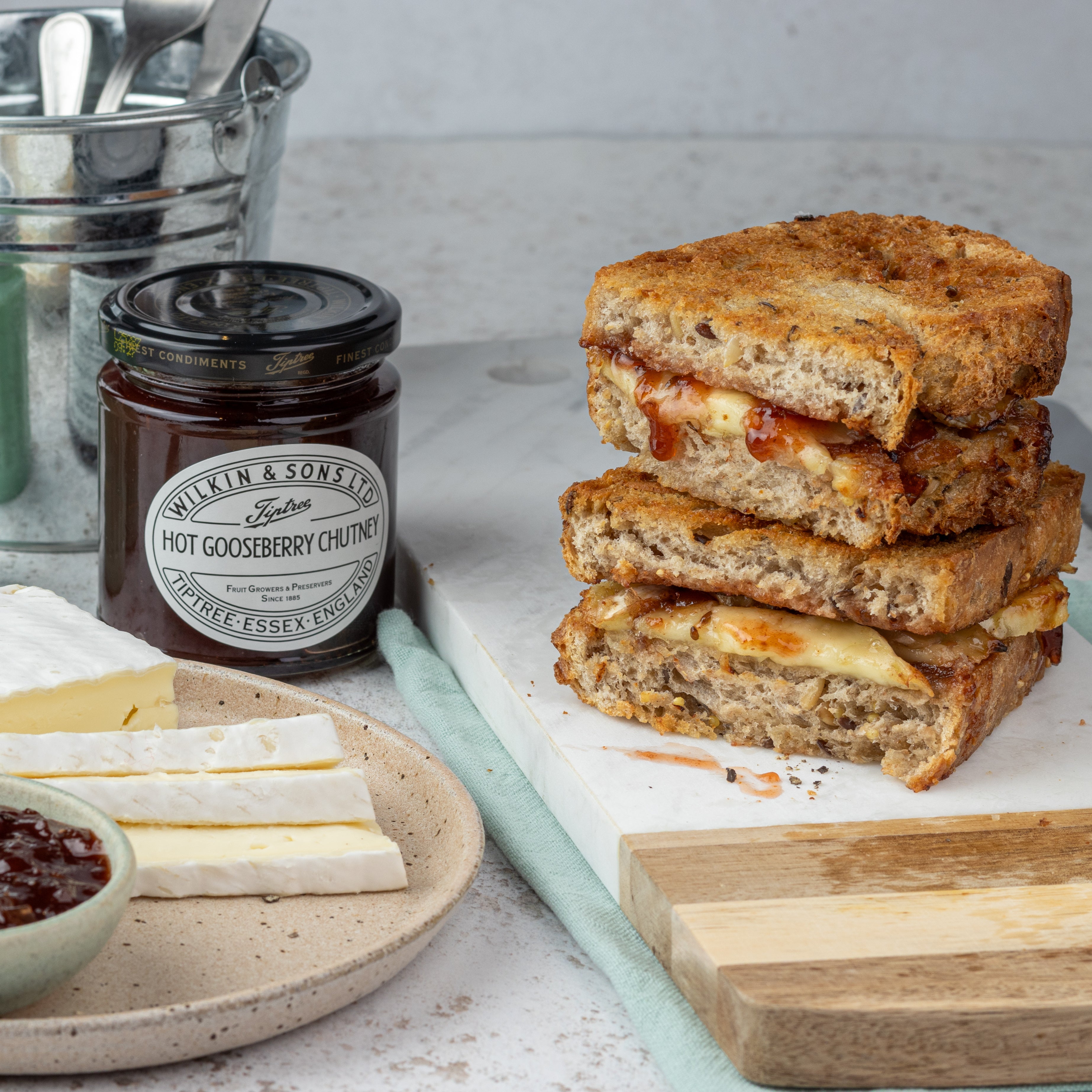 Stack of grilled sandwiches with cheese and chutney on a table with a jar of chutney.