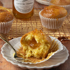 Muffin with a bite taken out on a plate with a fork, surrounded by other muffins and a bottle of 'Crystal Orange' marmalade.