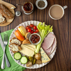 Platter of assorted meats, cheeses, and vegetables with a cup of coffee on a wooden table.