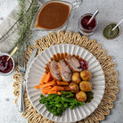 A beautifully styled holiday dinner plate featuring sliced roasted turkey, carrots, roasted potatoes, and broccoli, served on a white plate with gravy and Red Currant Jelly, set on a woven placemat.