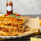Stack of quesadillas on a plate with a bottle of barbecue sauce in the background.