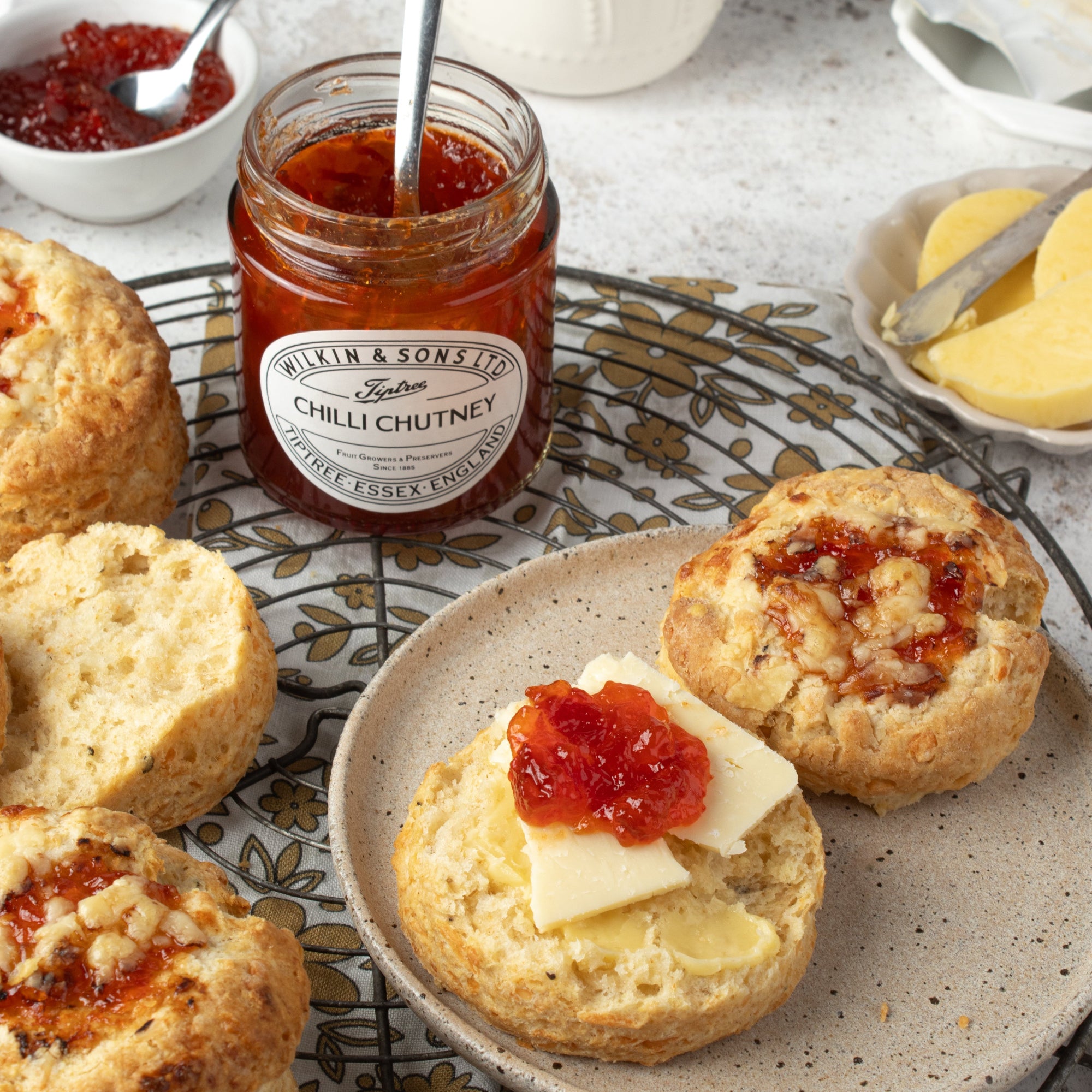 Scones with cheese, chutney and butter on a plate, accompanied by a jar of chutney.