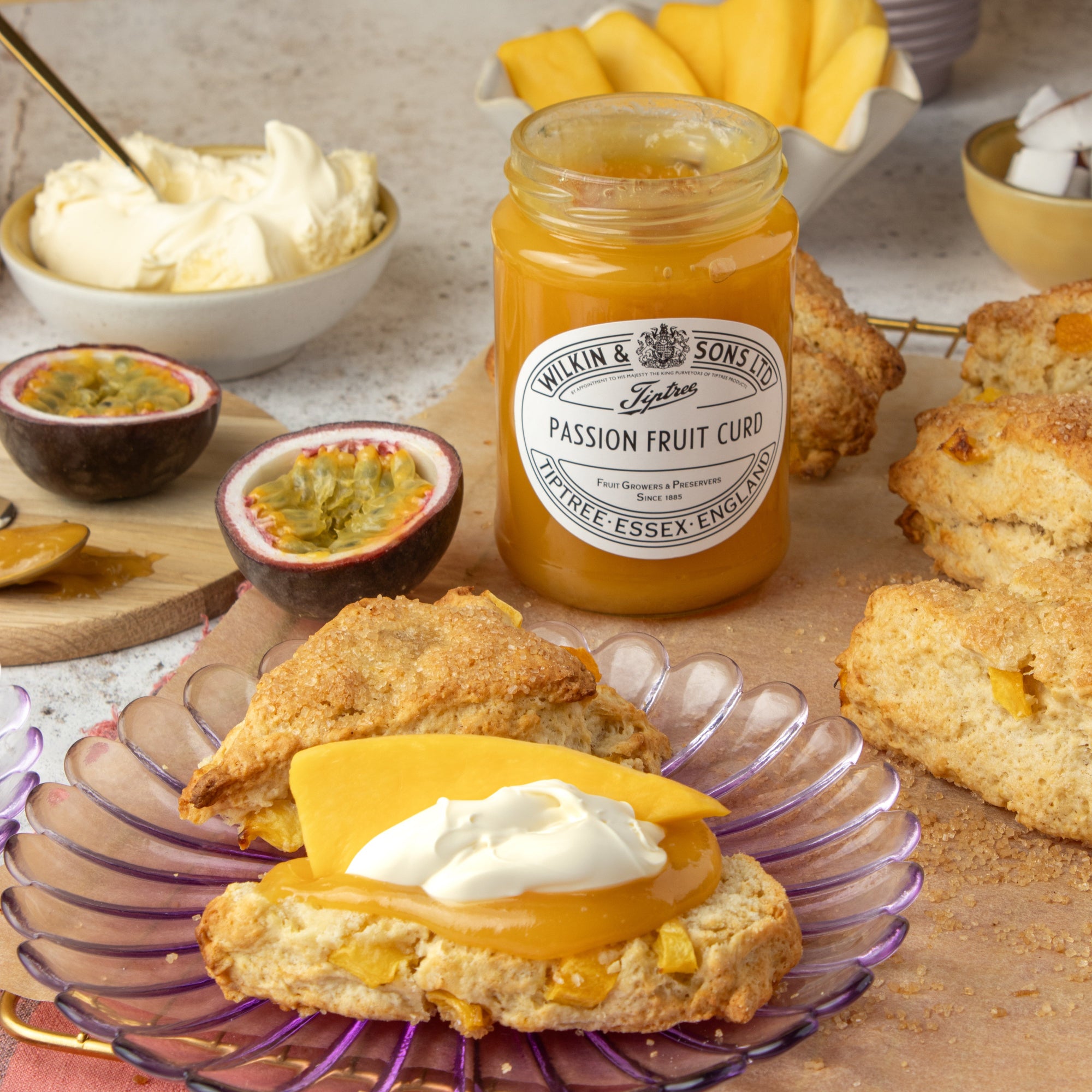 Mango and coconut scone with curd and cream on a plate with a jar of passion fruit curd in the background.