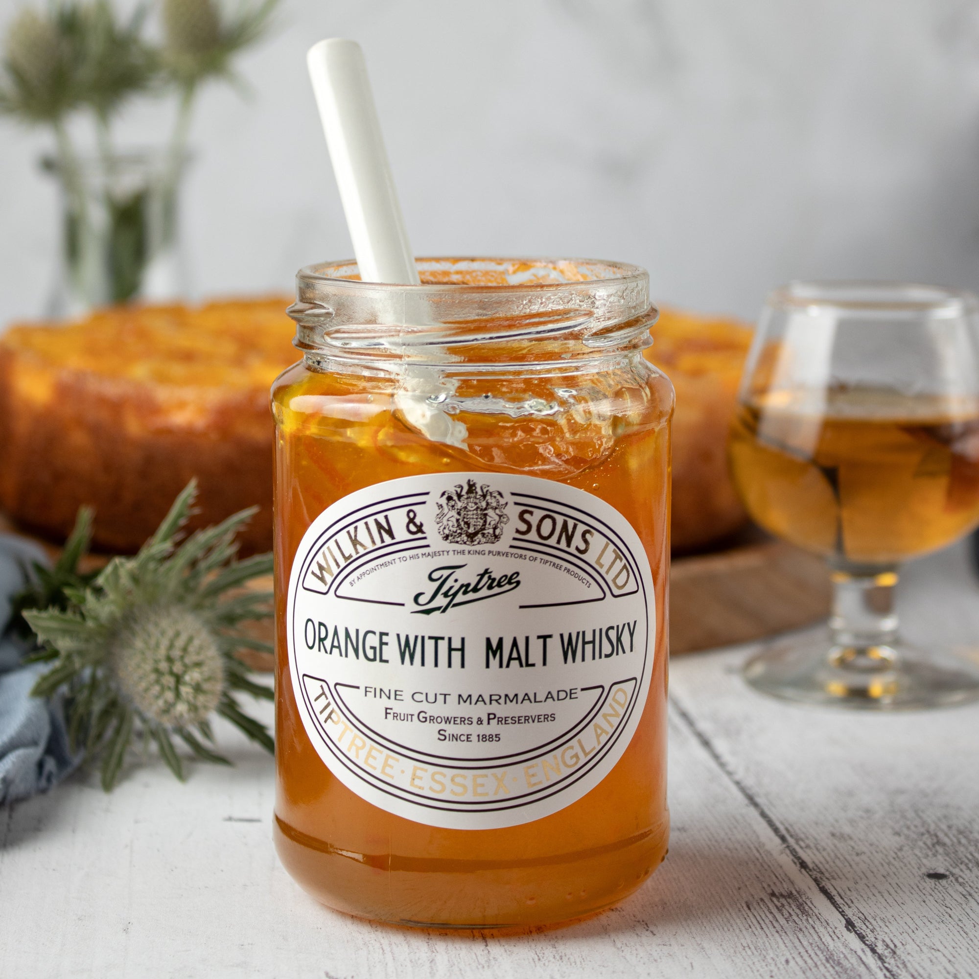 A jar of Tiptree Orange with Malt Whisky Marmalade with a cake and a glass of whisky in the background