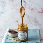 Jar of peanut butter with a spoon dripping peanut butter, on a light marble background.
