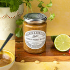 Jar of Wilkin & Sons Crunchy Peanut Butter on a wooden board with a lime and bowl of peanut butter.