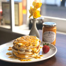 Stack of pancakes with Passion Fruit Curd, a strawberry, and a jar of Passion Fruit Curd on a plate.
