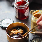 Person using a spoon to stir a mixture of Cumberland sauce and mustard in a bowl on a wooden surface.