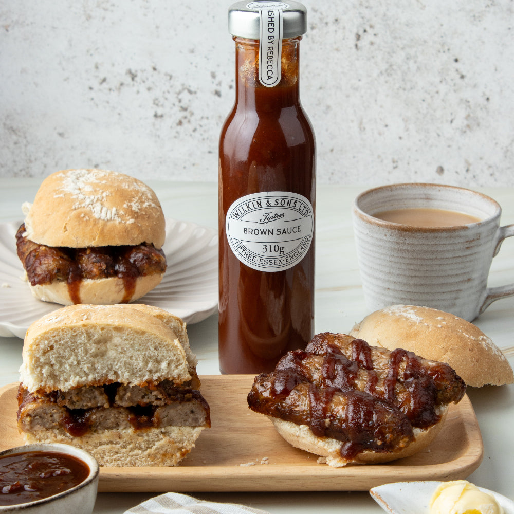 Bottle of brown sauce with sandwiches and a cup of coffee on a wooden board.