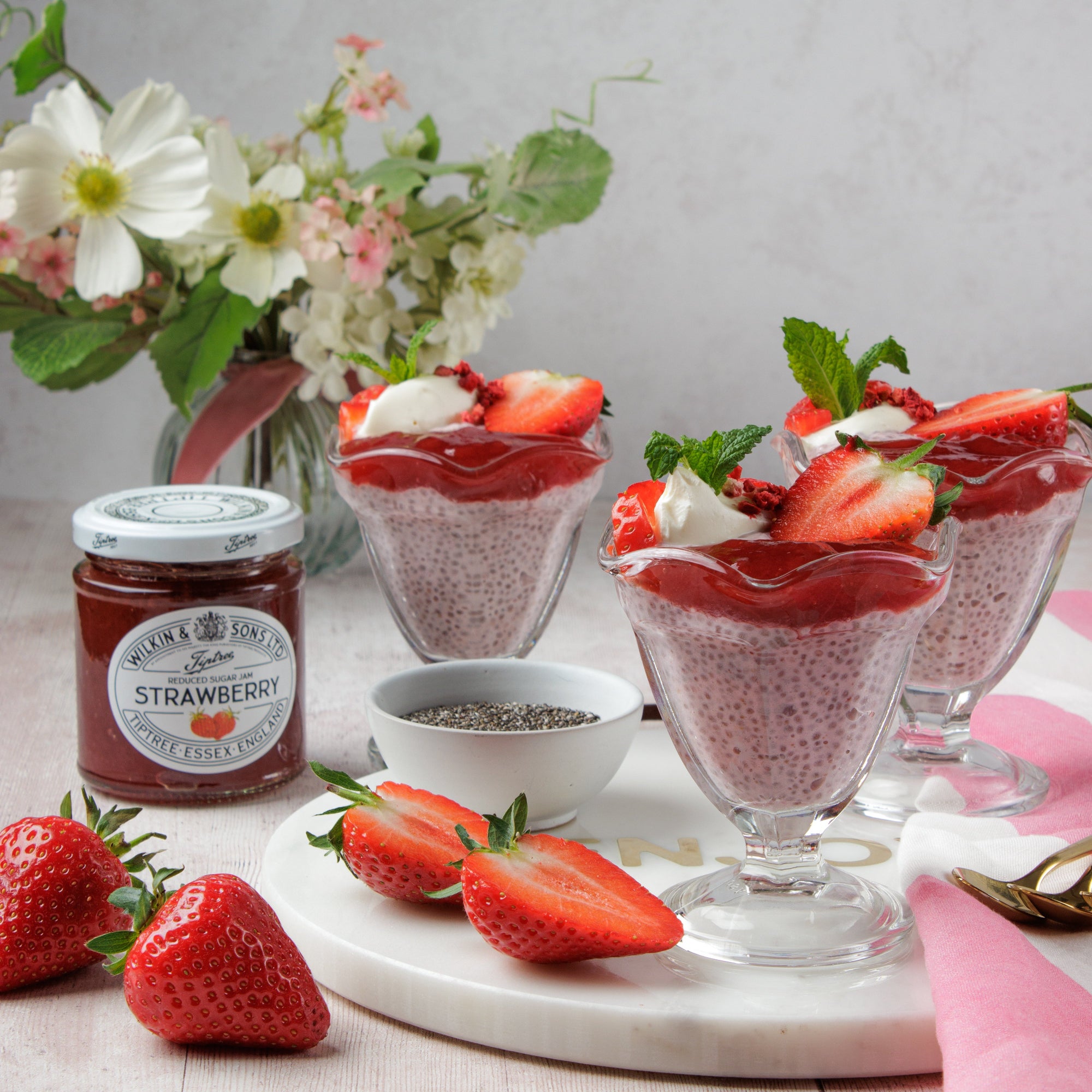 Strawberry dessert with chia seeds, fresh strawberries, and a jar of strawberry jam on a table.