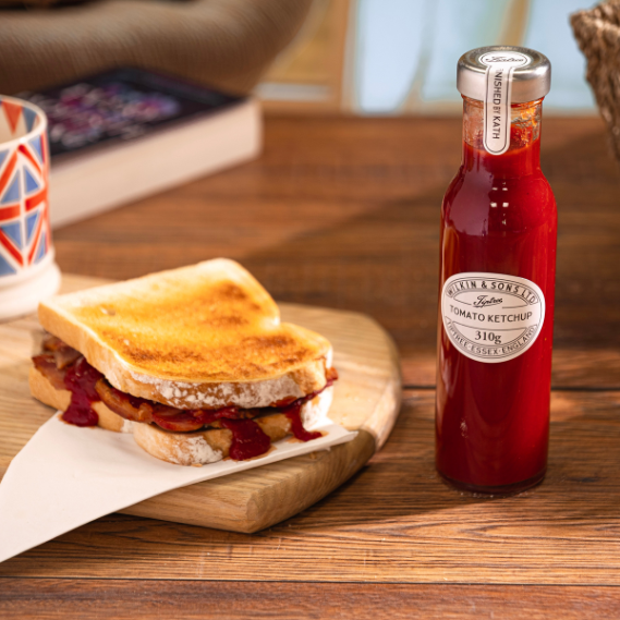 Tiptree tomato ketchup bottle next to a toasted sandwich on a wooden table